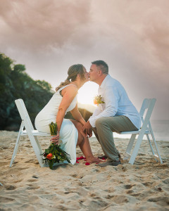 Newlyweds sharing a kiss at sunset on Carambola Beach, St. Croix, golden light reflecting off the calm ocean.