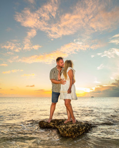 Romantic kiss between engaged couple on rocky coastline with crashing waves