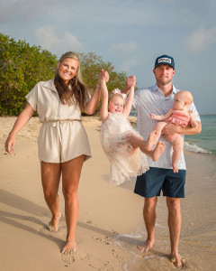 Parents and children walking hand in hand along a sandy beach during golden hour.