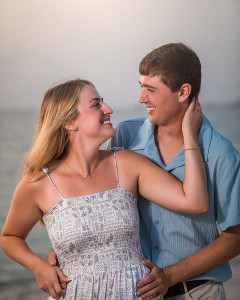 Couple sharing an intimate moment as the sun sets over the ocean during an engagement session.