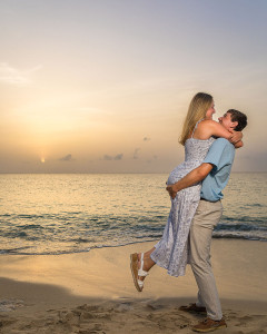 Couple hugging against a colorful sunset sky on a sandy beach.