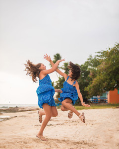 Sisters jumping and having fun on a white sand beach with the Caribbean Sea behind them.