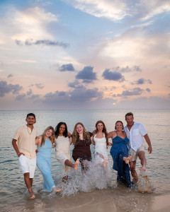 Happy family holding each other along a white sand beach at sunset in St. Croix, with turquoise Caribbean waters and golden light creating a warm tropical backdrop.