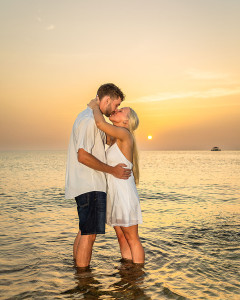 Couple embracing on the beach with the sun setting behind them, casting warm golden light.