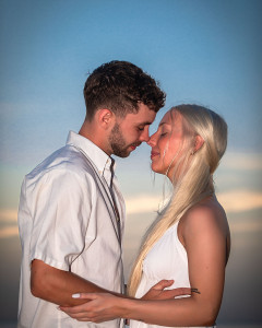 Close-up of a couple sharing a soft kiss on the beach at sunset with ocean waves in the background.